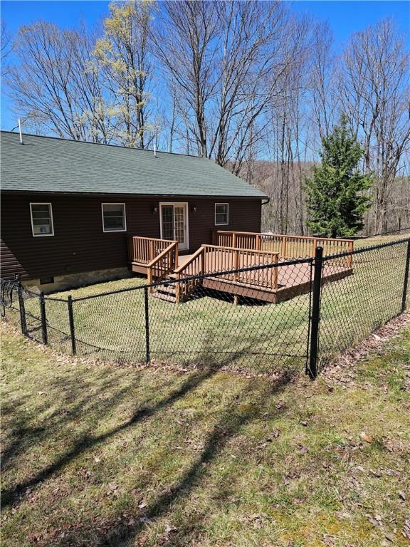 rear view of property featuring fence, a wooden deck, a shingled roof, and a yard
