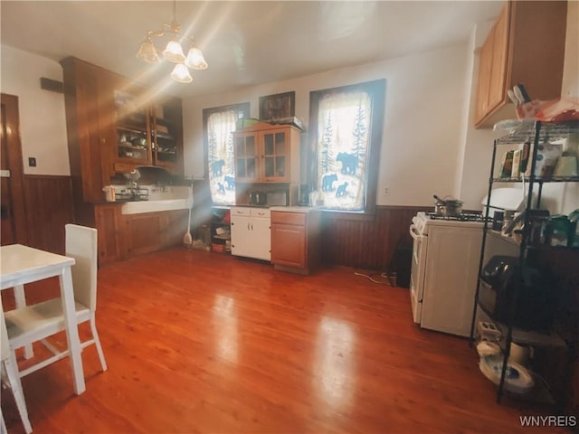 kitchen with glass insert cabinets, wood walls, a chandelier, a wainscoted wall, and wood finished floors