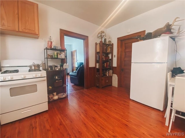 kitchen featuring a wainscoted wall, wood finished floors, and white appliances