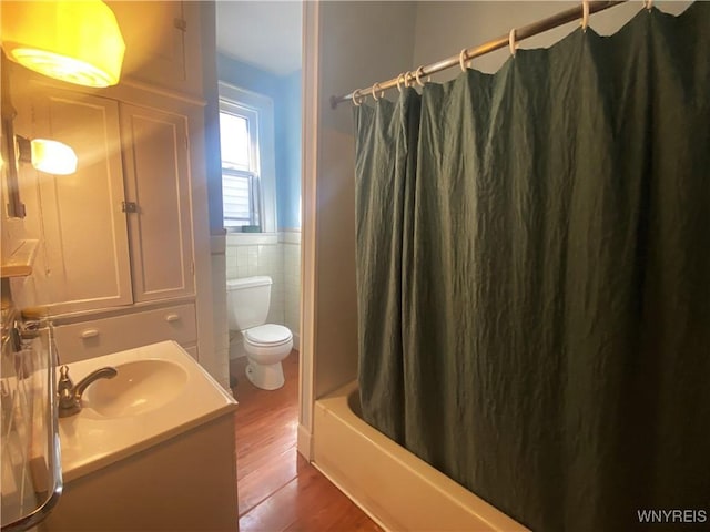 bathroom featuring toilet, tile walls, wood finished floors, vanity, and wainscoting