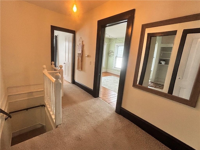 hall featuring an upstairs landing, light colored carpet, and baseboards