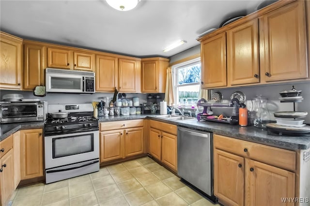 kitchen featuring a toaster, dark countertops, a sink, light tile patterned floors, and stainless steel appliances