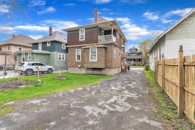 exterior space featuring a balcony, a residential view, a lawn, brick siding, and fence