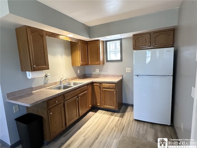 kitchen with brown cabinets, a sink, light wood-style flooring, baseboards, and freestanding refrigerator