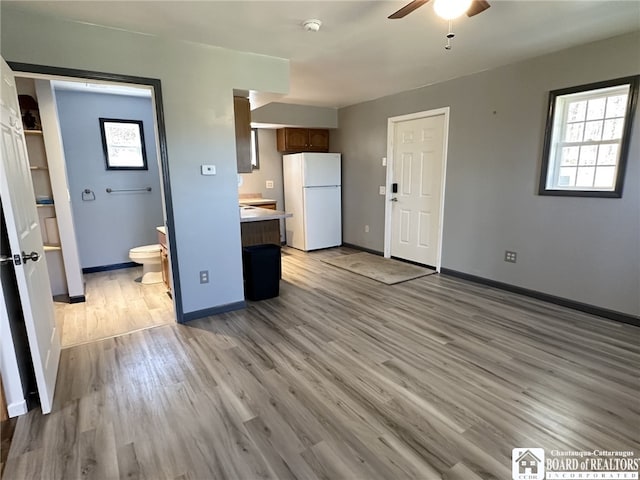 unfurnished living room featuring light wood-style floors, plenty of natural light, a ceiling fan, and baseboards