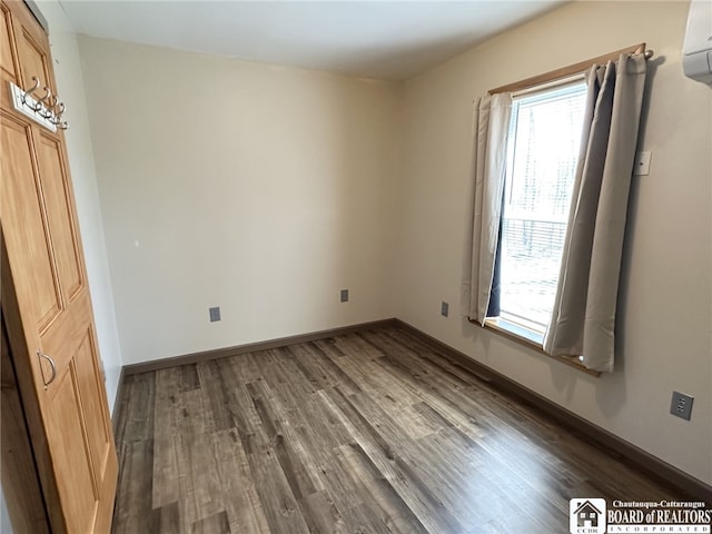 interior space with a wall mounted air conditioner, multiple windows, wood finished floors, and baseboards