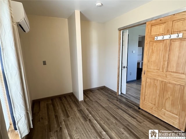 empty room with a wall mounted AC, dark wood-style floors, and baseboards
