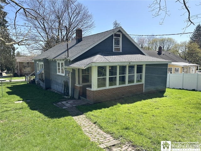 rear view of house featuring a chimney, brick siding, fence, a shingled roof, and a lawn