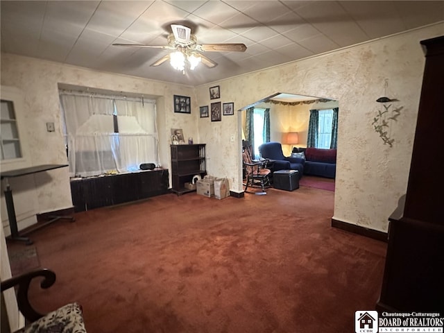 carpeted living area featuring baseboards, a ceiling fan, and a healthy amount of sunlight
