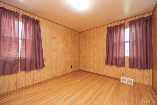 spare room with wood walls, wood finished floors, visible vents, and baseboards