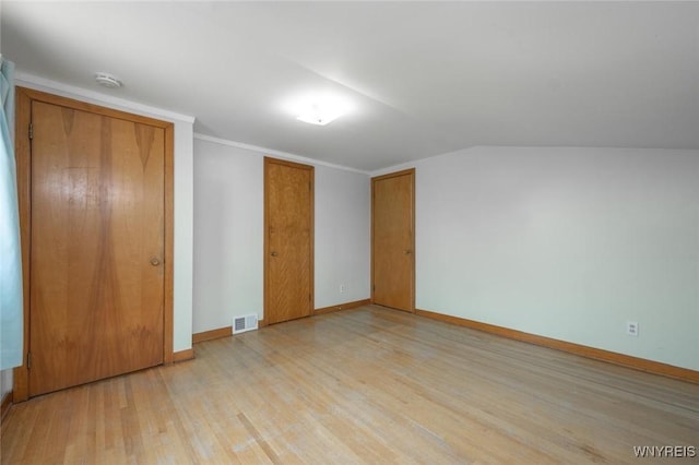 unfurnished bedroom featuring baseboards, visible vents, light wood-style floors, and vaulted ceiling