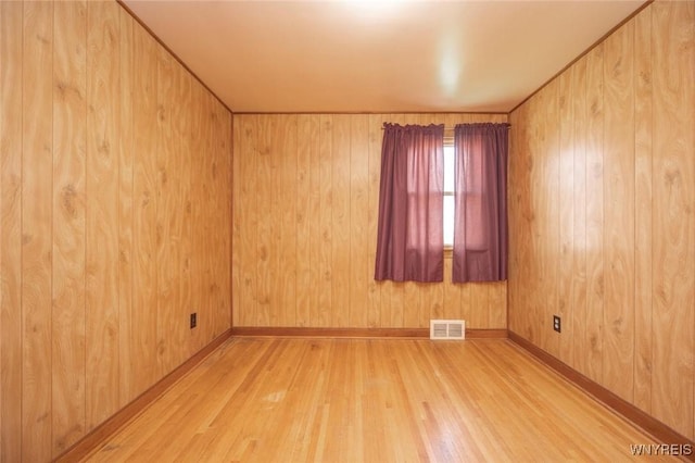 empty room featuring wooden walls, visible vents, and wood finished floors