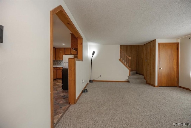 unfurnished living room featuring baseboards, stairway, a textured ceiling, and light colored carpet
