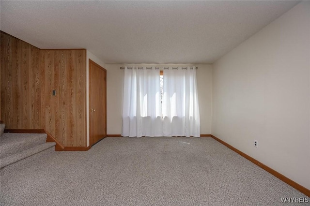 carpeted spare room with wood walls, stairs, and baseboards