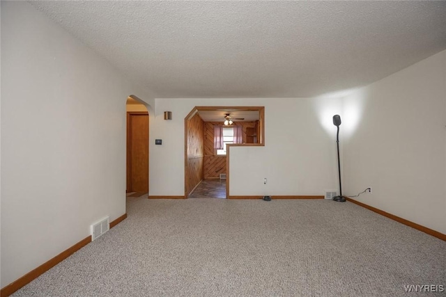 unfurnished room featuring arched walkways, carpet flooring, baseboards, visible vents, and a textured ceiling
