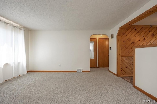 unfurnished room featuring a textured ceiling, visible vents, carpet flooring, and arched walkways