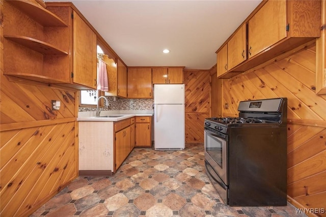 kitchen featuring a sink, wooden walls, light countertops, freestanding refrigerator, and gas range