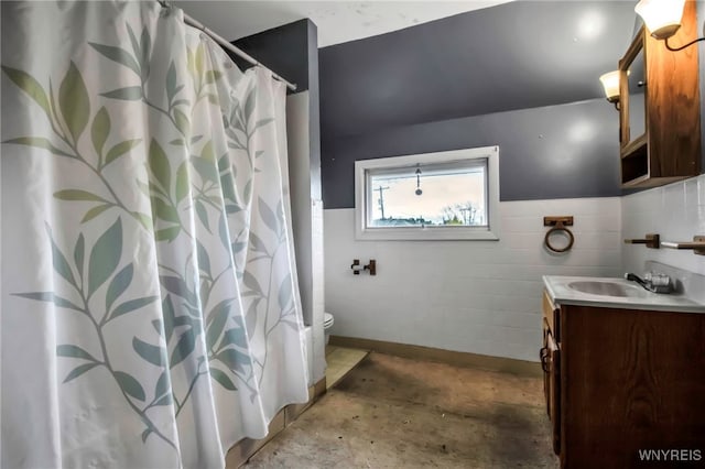 bathroom featuring concrete floors, tile walls, a wainscoted wall, toilet, and vanity