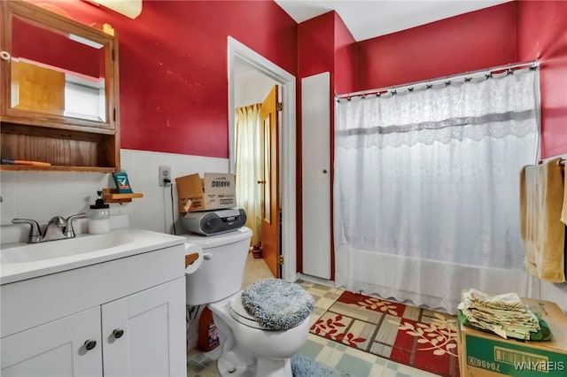 full bathroom with tile walls, vanity, tile patterned floors, toilet, and a wainscoted wall