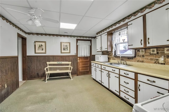 kitchen featuring a sink, white microwave, light carpet, light countertops, and wainscoting