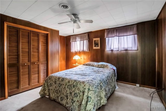 carpeted bedroom with wooden walls, a closet, and a ceiling fan