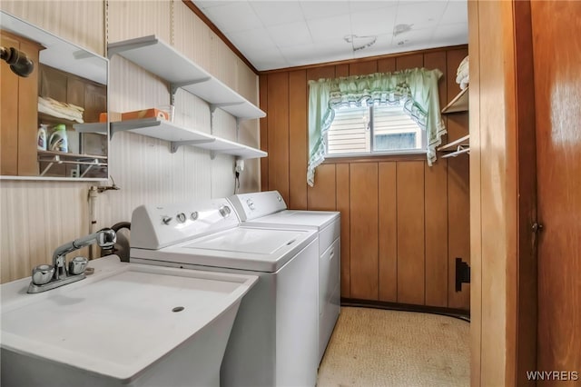 washroom featuring independent washer and dryer, wooden walls, laundry area, and a sink