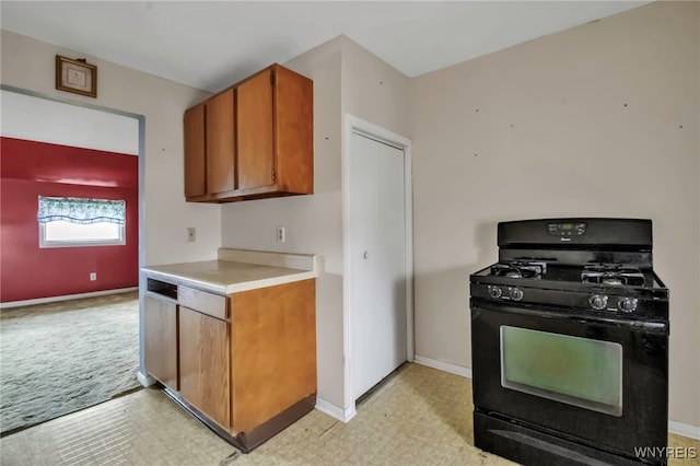 kitchen featuring light floors, brown cabinetry, light countertops, baseboards, and black range with gas cooktop