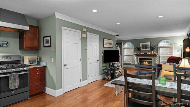 dining space featuring crown molding, light wood-style flooring, a glass covered fireplace, and baseboards