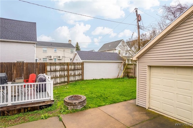 view of yard with a wooden deck, an outbuilding, a garage, a fenced backyard, and a fire pit