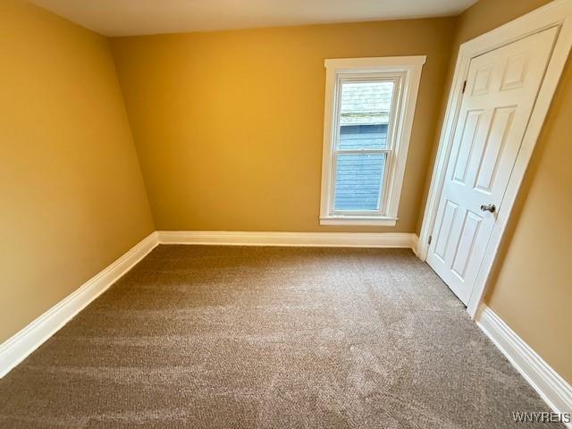 empty room featuring baseboards and dark colored carpet