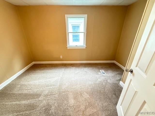 unfurnished room with carpet, visible vents, and baseboards