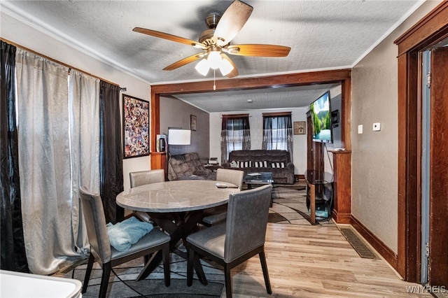 dining area featuring a textured ceiling, ceiling fan, a textured wall, baseboards, and light wood-type flooring