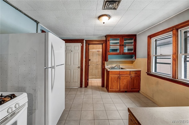 kitchen with light tile patterned floors, visible vents, glass insert cabinets, and a sink