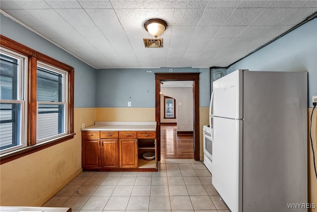 kitchen featuring brown cabinetry, light tile patterned floors, white appliances, and light countertops