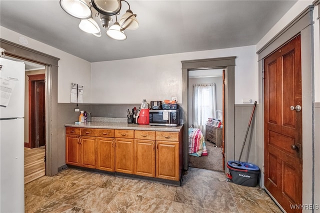 kitchen with stainless steel microwave, brown cabinets, a chandelier, light countertops, and freestanding refrigerator