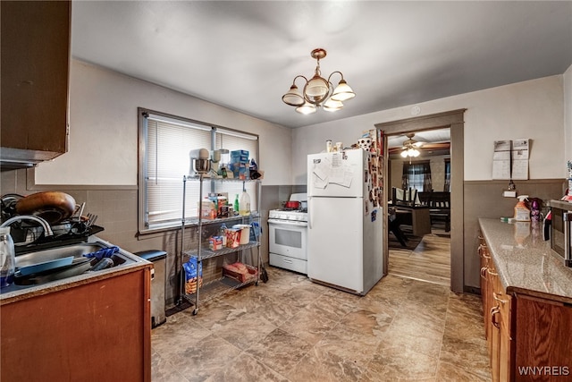kitchen featuring white appliances, brown cabinets, ceiling fan with notable chandelier, a wainscoted wall, and a sink