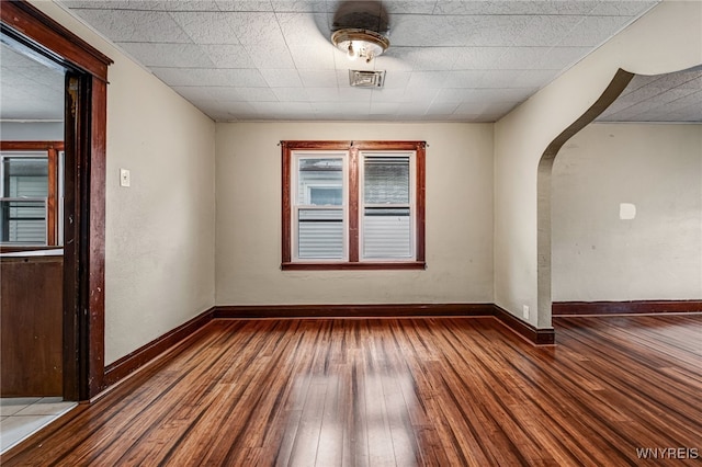 empty room with baseboards, visible vents, hardwood / wood-style flooring, and arched walkways