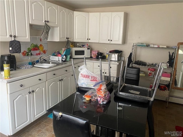 kitchen with tasteful backsplash, a sink, light countertops, white cabinets, and white microwave
