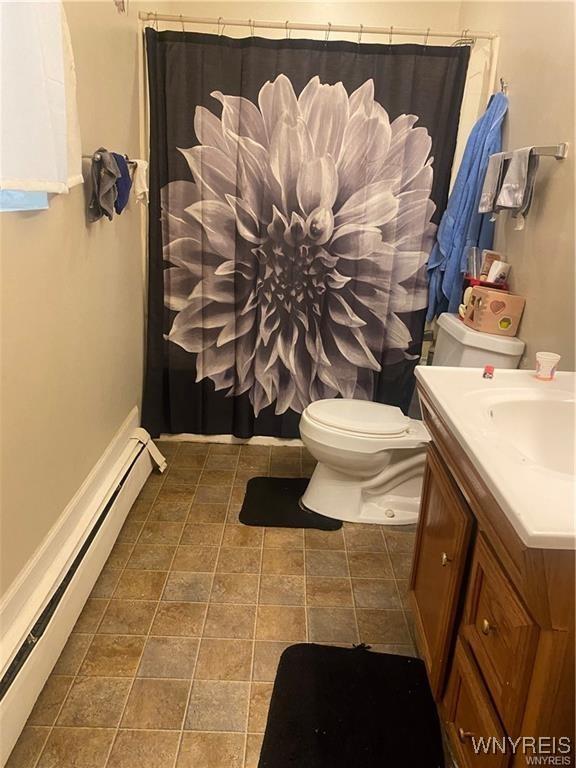 full bath featuring baseboard heating, curtained shower, vanity, baseboards, and toilet