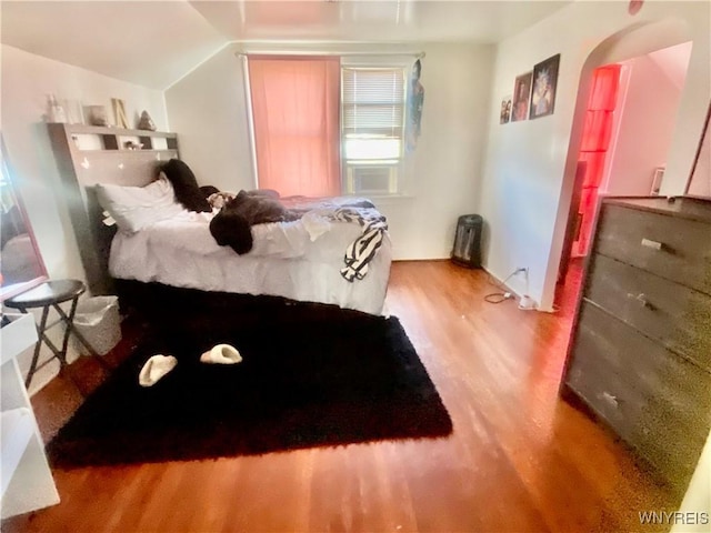 bedroom featuring arched walkways, wood finished floors, and vaulted ceiling