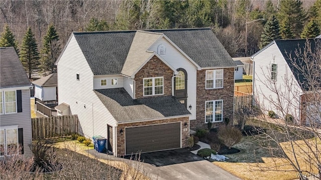 traditional-style house featuring fence, a shingled roof, driveway, and stone siding