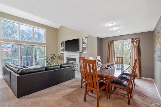 dining room featuring baseboards, a glass covered fireplace, and light carpet