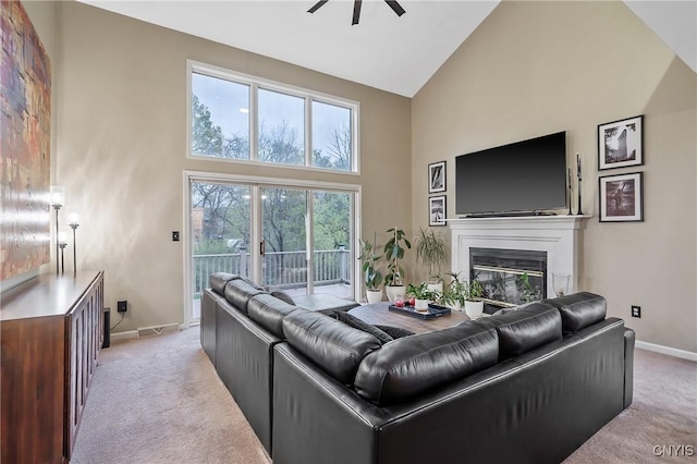 living area with a glass covered fireplace, light carpet, baseboards, high vaulted ceiling, and a ceiling fan
