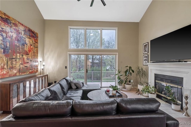 living area featuring ceiling fan, a fireplace with flush hearth, and a towering ceiling