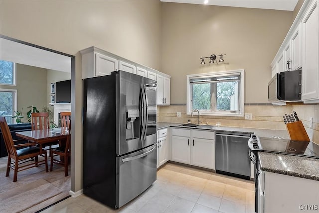 kitchen with decorative backsplash, a towering ceiling, white cabinets, a sink, and stainless steel appliances