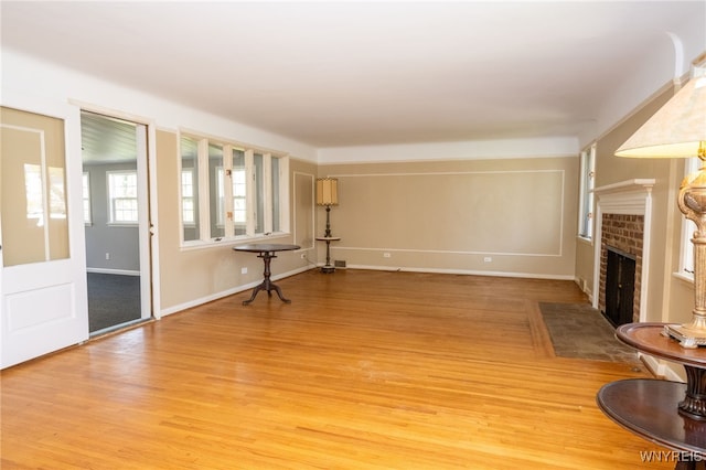 unfurnished living room with a brick fireplace, baseboards, and light wood-type flooring