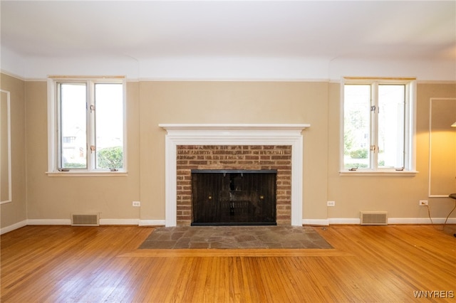 unfurnished living room with a brick fireplace, visible vents, and wood finished floors