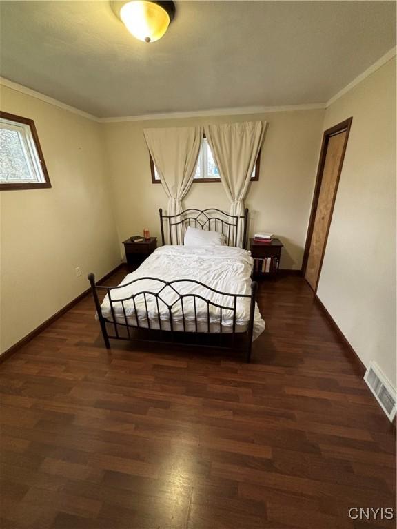 bedroom with baseboards, visible vents, ornamental molding, and wood finished floors