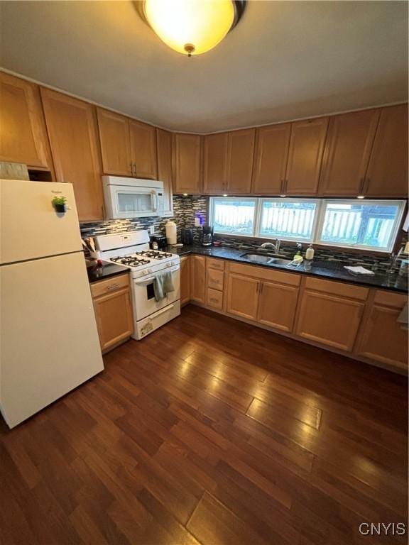 kitchen featuring decorative backsplash, dark countertops, white appliances, dark wood-type flooring, and a sink