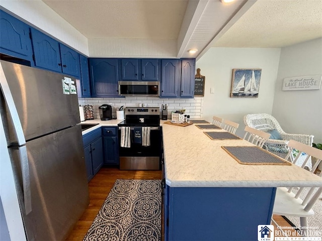 kitchen with dark wood finished floors, blue cabinetry, appliances with stainless steel finishes, light countertops, and a kitchen bar